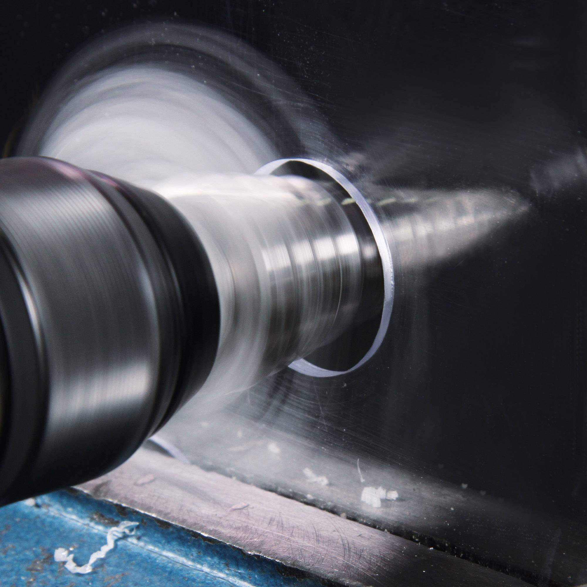 Eine drehende Metallbohrmaschine durchbohrt eine silberne Metallplatte und erzeugt einen kreisförmigen Schnitt.