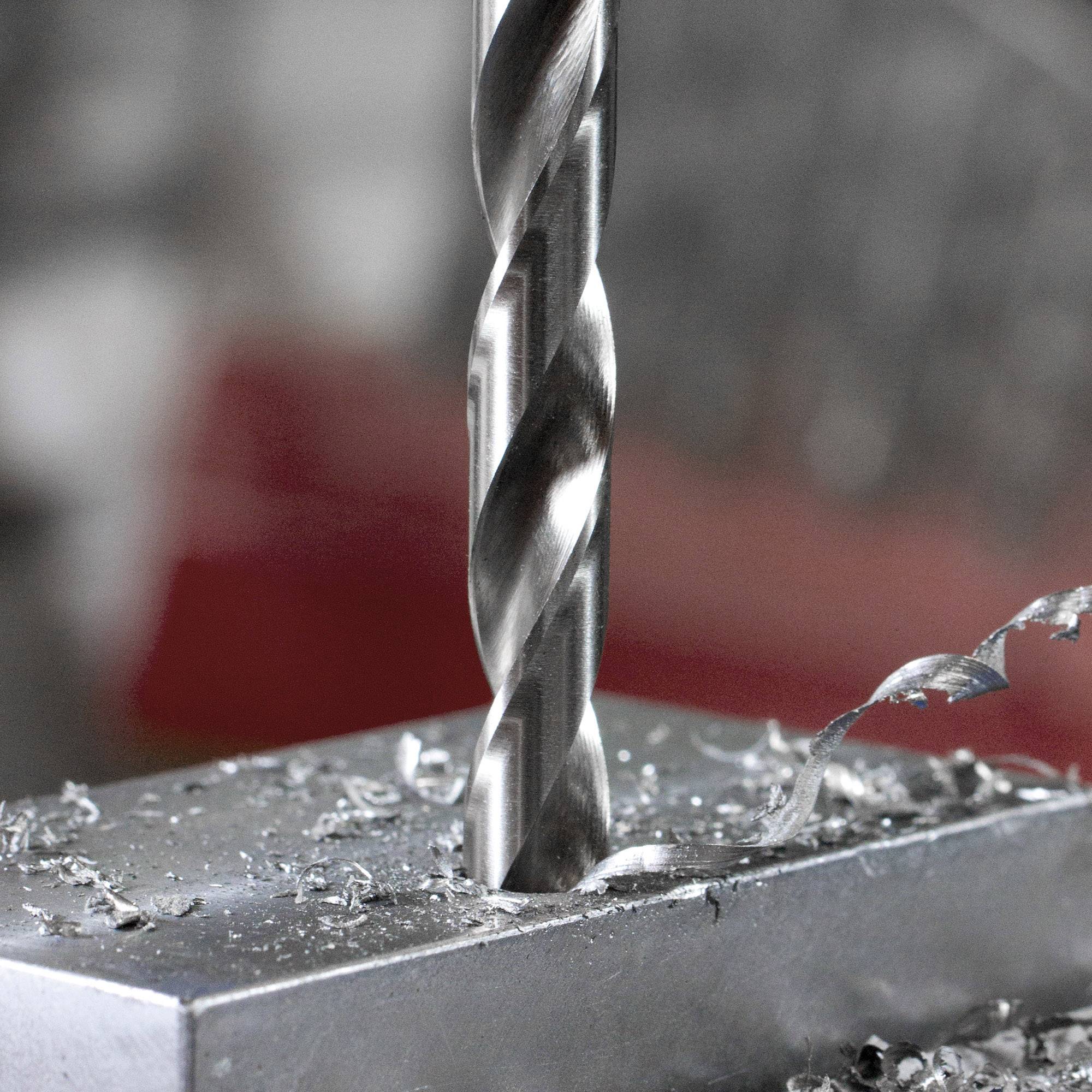 Nahaufnahme eines Bohrers, der ein Loch in ein Metallstück bohrt. Metallspäne sind um das Bohrloch herum zu sehen, im Hintergrund unscharf.
