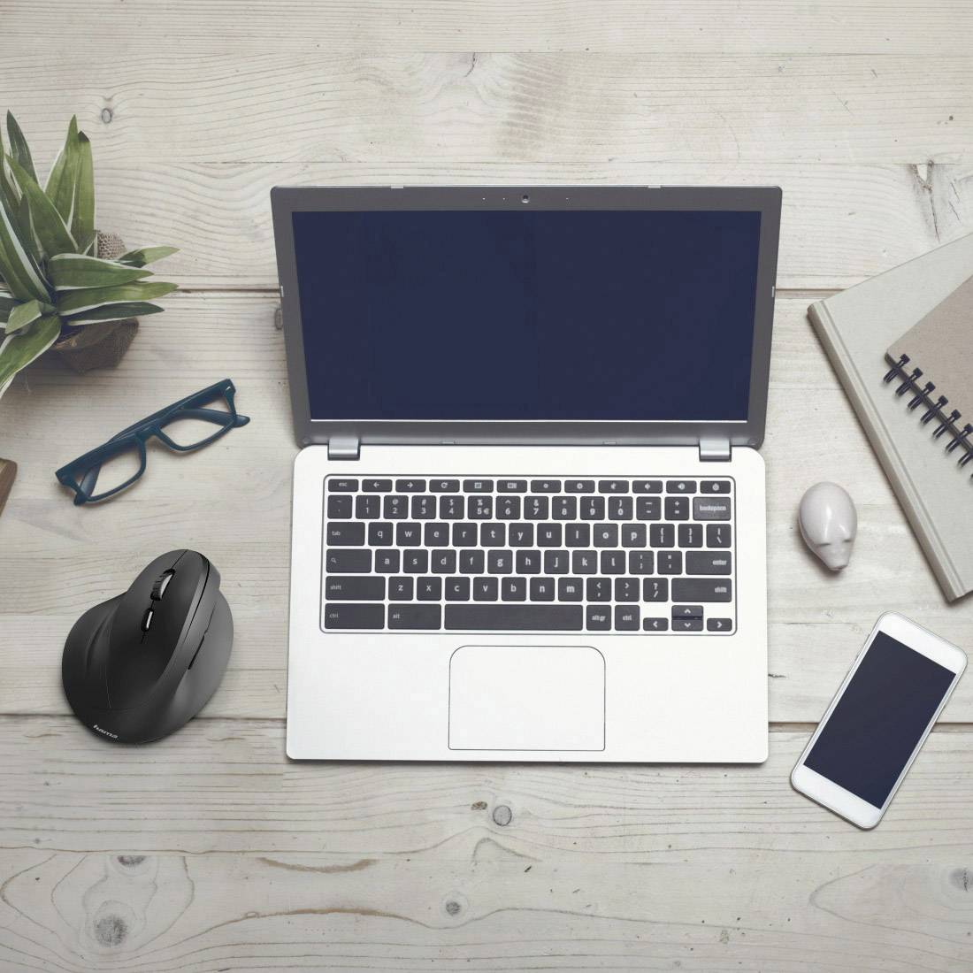 Laptop auf Holztisch mit Zubehör: Smartphone, Maus, Brille, Pflanze. Büroarbeitsplatz mit neutralem Hintergrund.