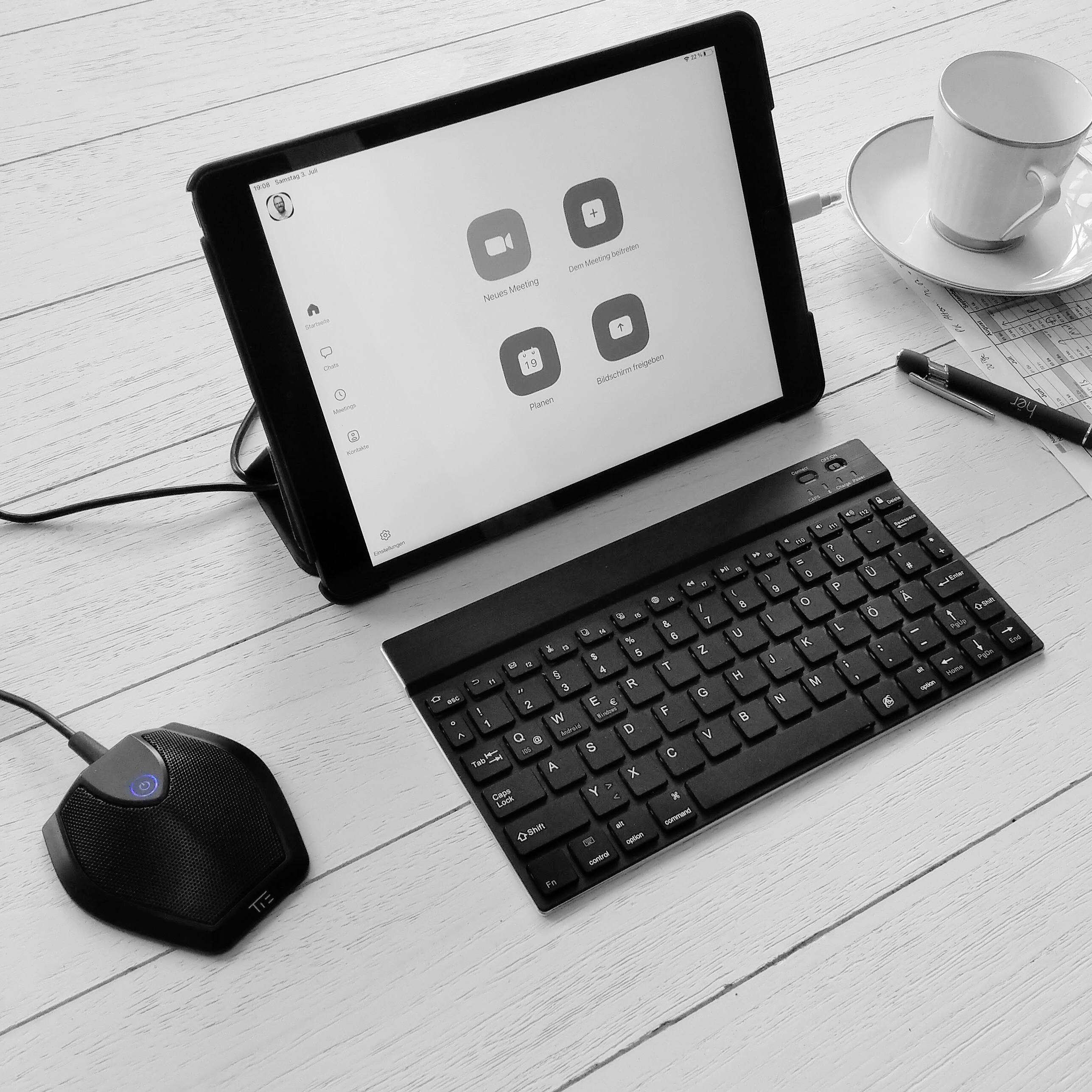 Tablet mit geöffneter Videokonferenz-App, kabellose Tastatur und Tasse Tee auf einem Tisch. Bereit für einen virtuellen Anruf.