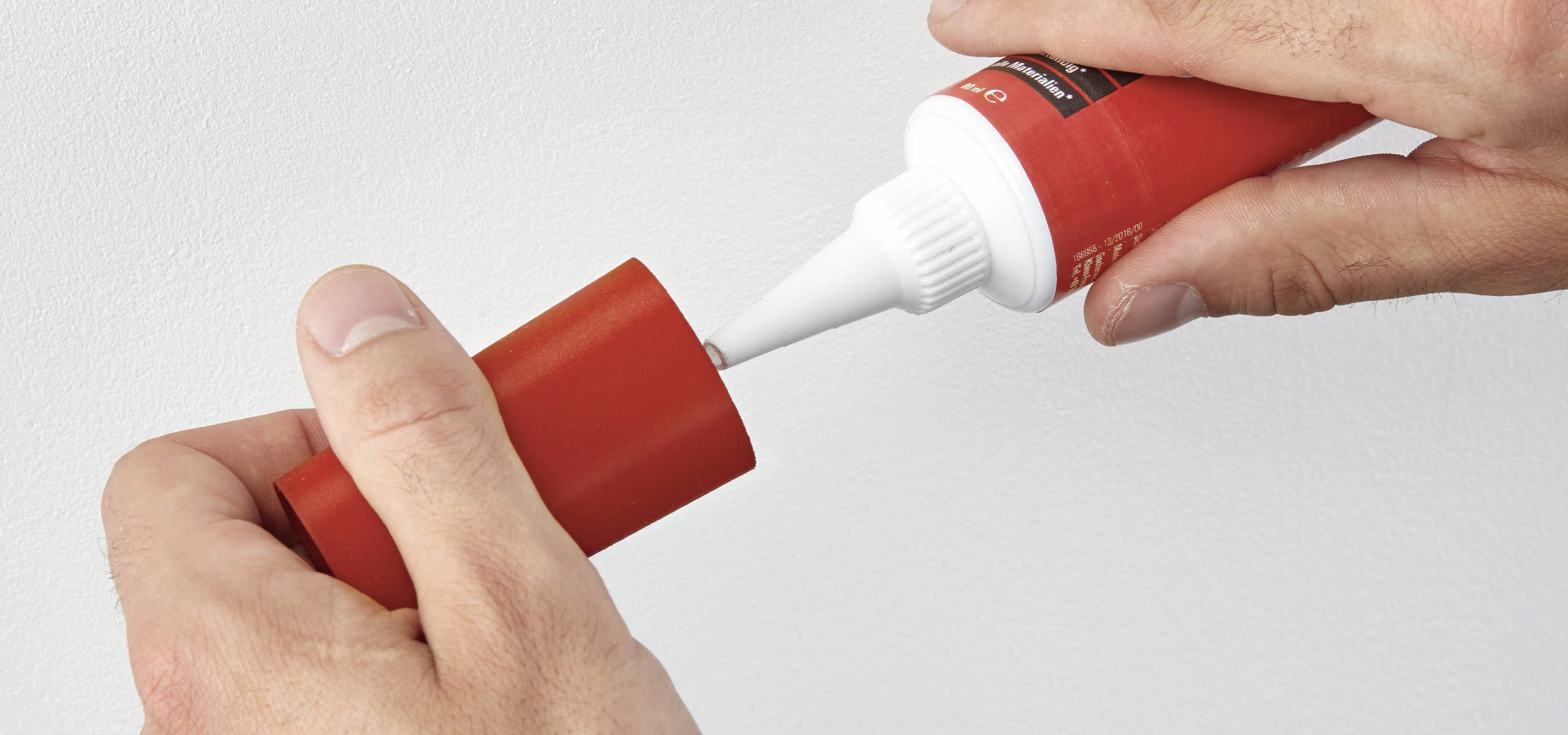 Zwei Hände öffnen eine rote Tube mit weißer Spitze und entfernen die Kappe.