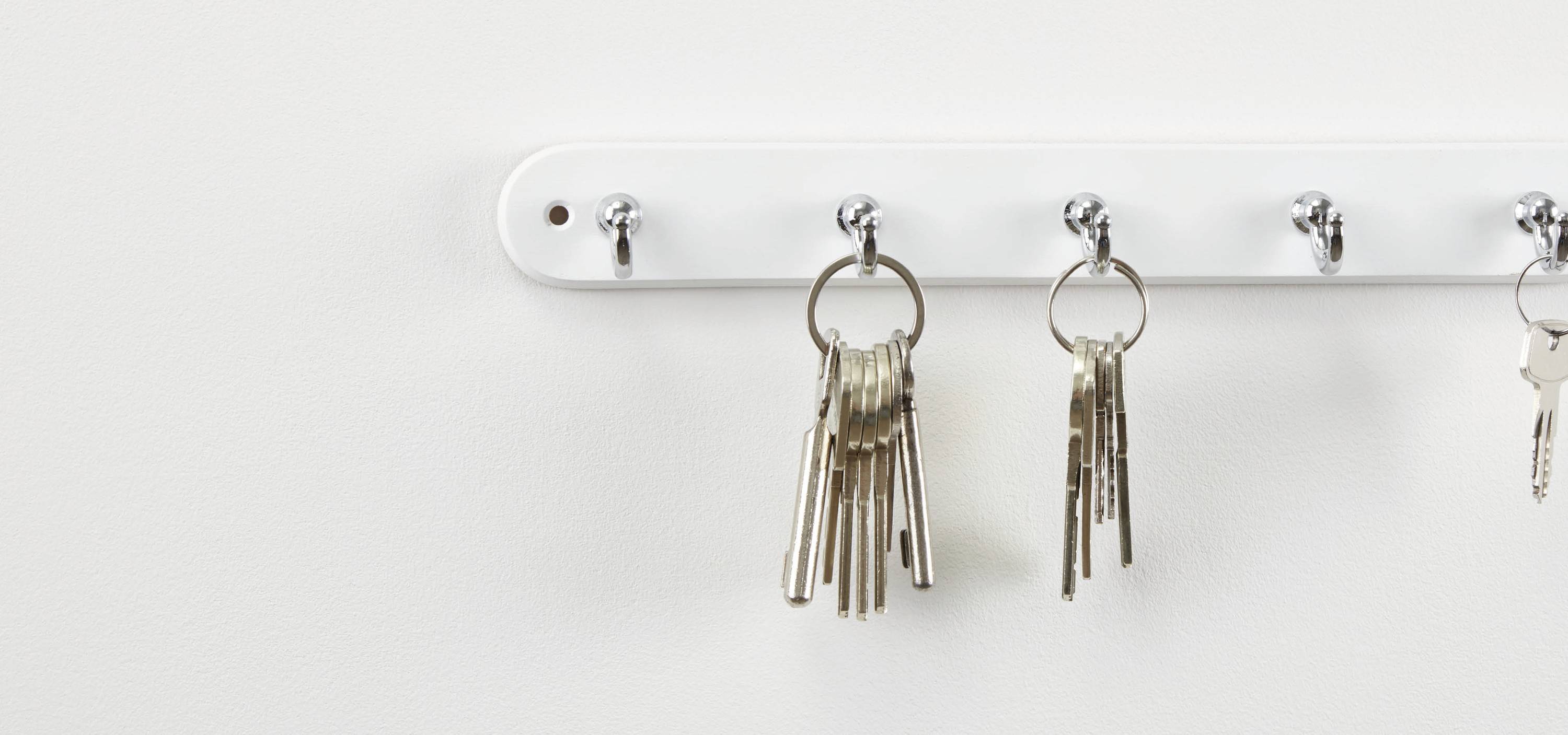 Ein weißes Wandregal mit mehreren Haken, an denen verschiedene Schlüsselbunde hängen.