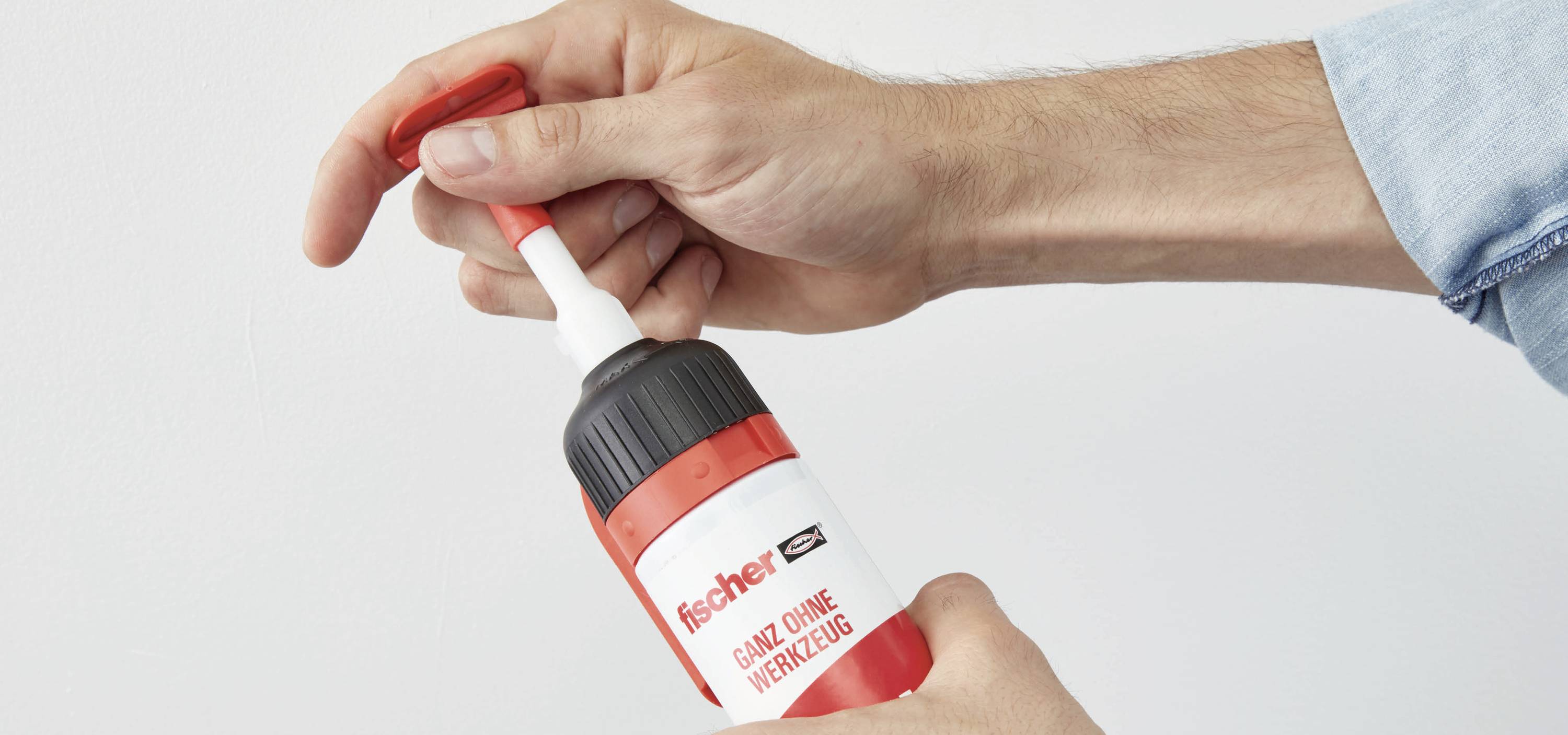 Eine Hand drückt Klebstoff aus einer roten Flasche mit der Aufschrift 'fischer - Ganz ohne Werkzeug'.