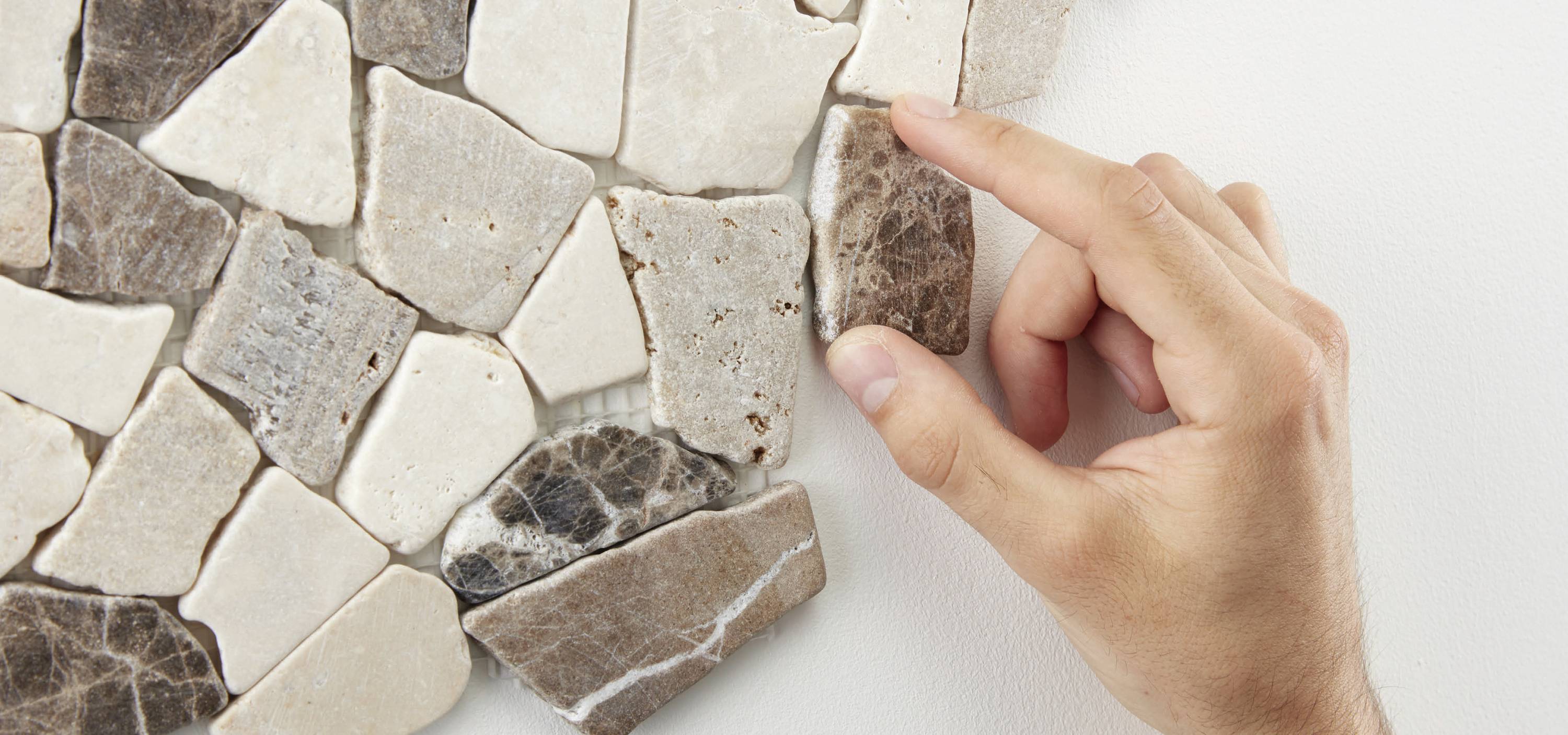 Hand platziert Steinmosaikstück an Wand; creme und braunes Farbschema, feine Details dekoration betonend.