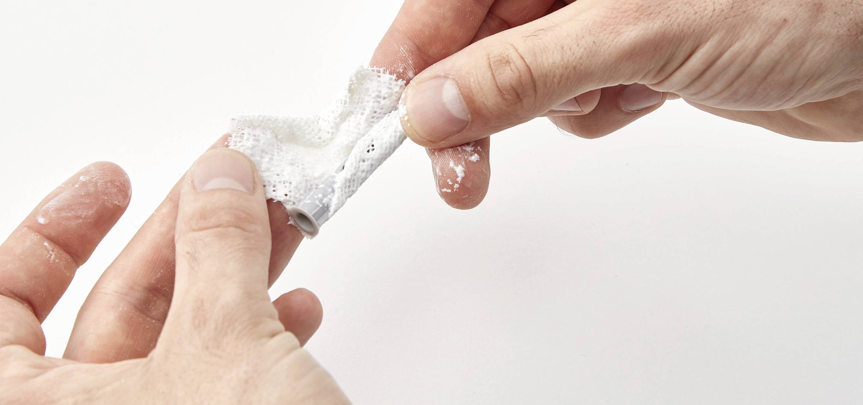 Eine Hand dreht ein zerknittertes weißes Tuch, während die andere hält. Rückstände von weißem Pulver sind zu sehen.