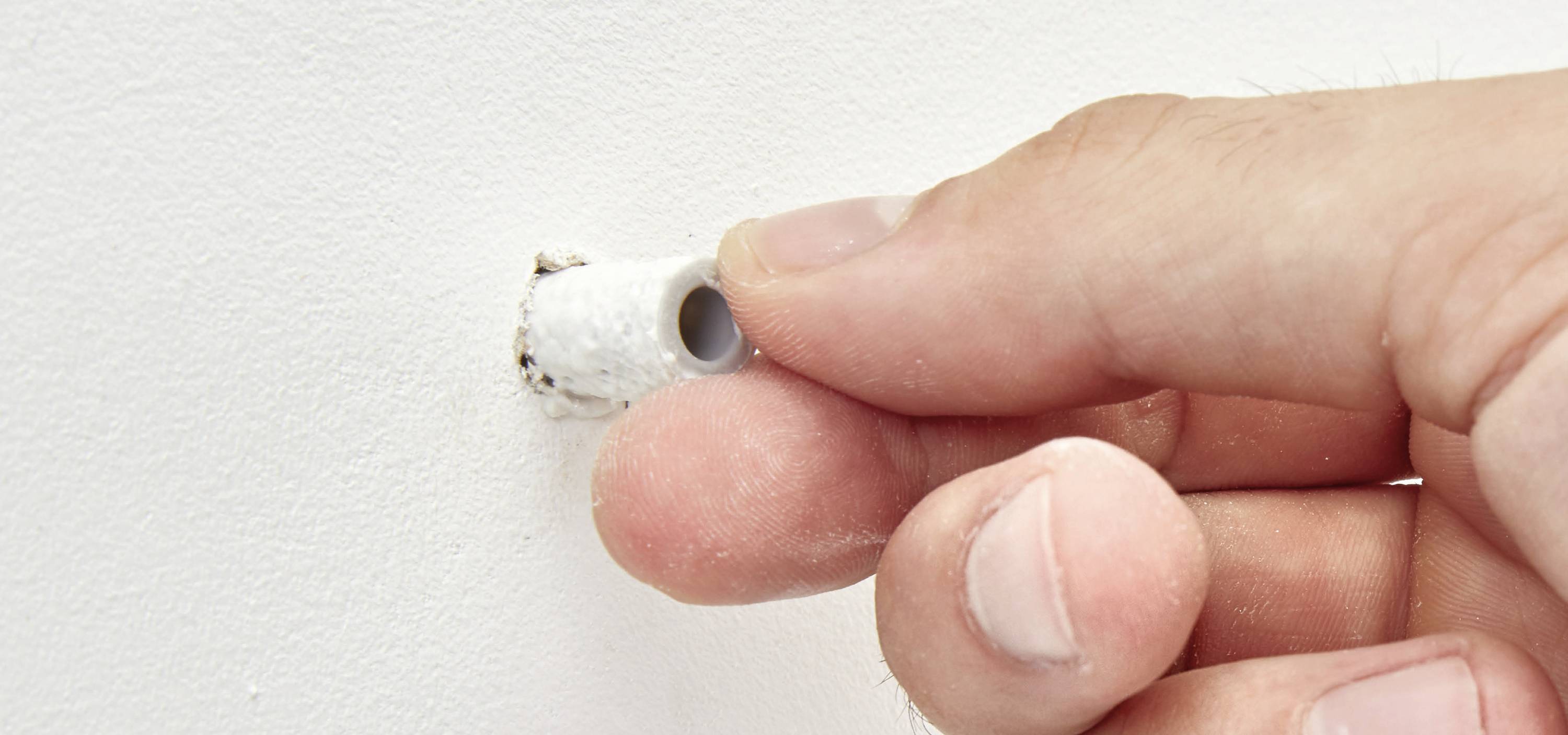 Jemand steckt einen Dübel in ein Loch in der Wand.