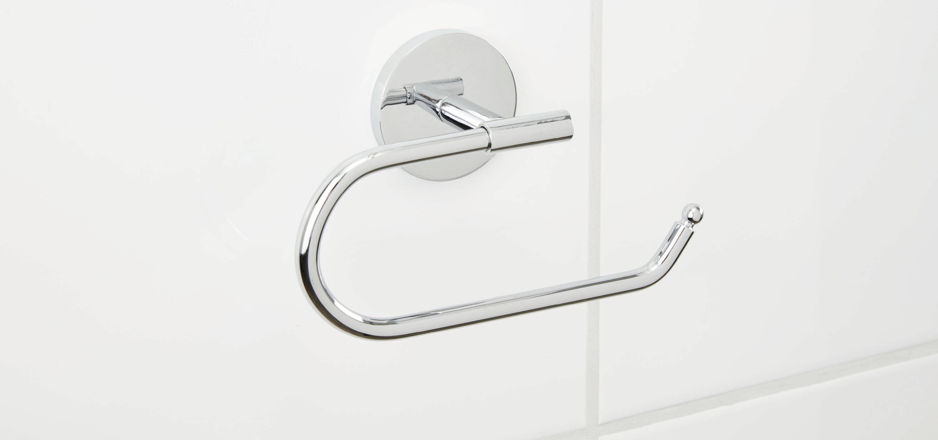 Ein leerer, verchromter Toilettenpapierhalter an einer weißen Badezimmerwand.