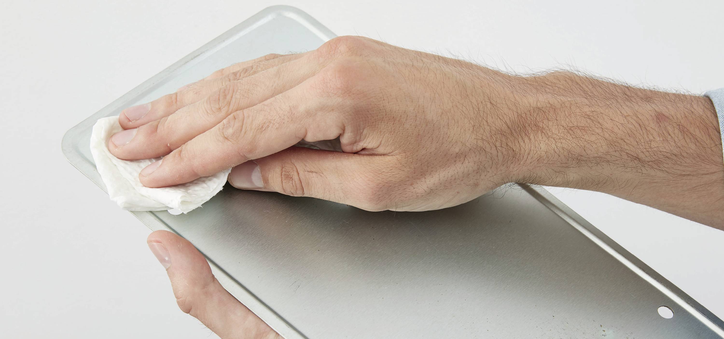 Eine Hand reinigt mit einem weißen Tuch eine Metalloberfläche.