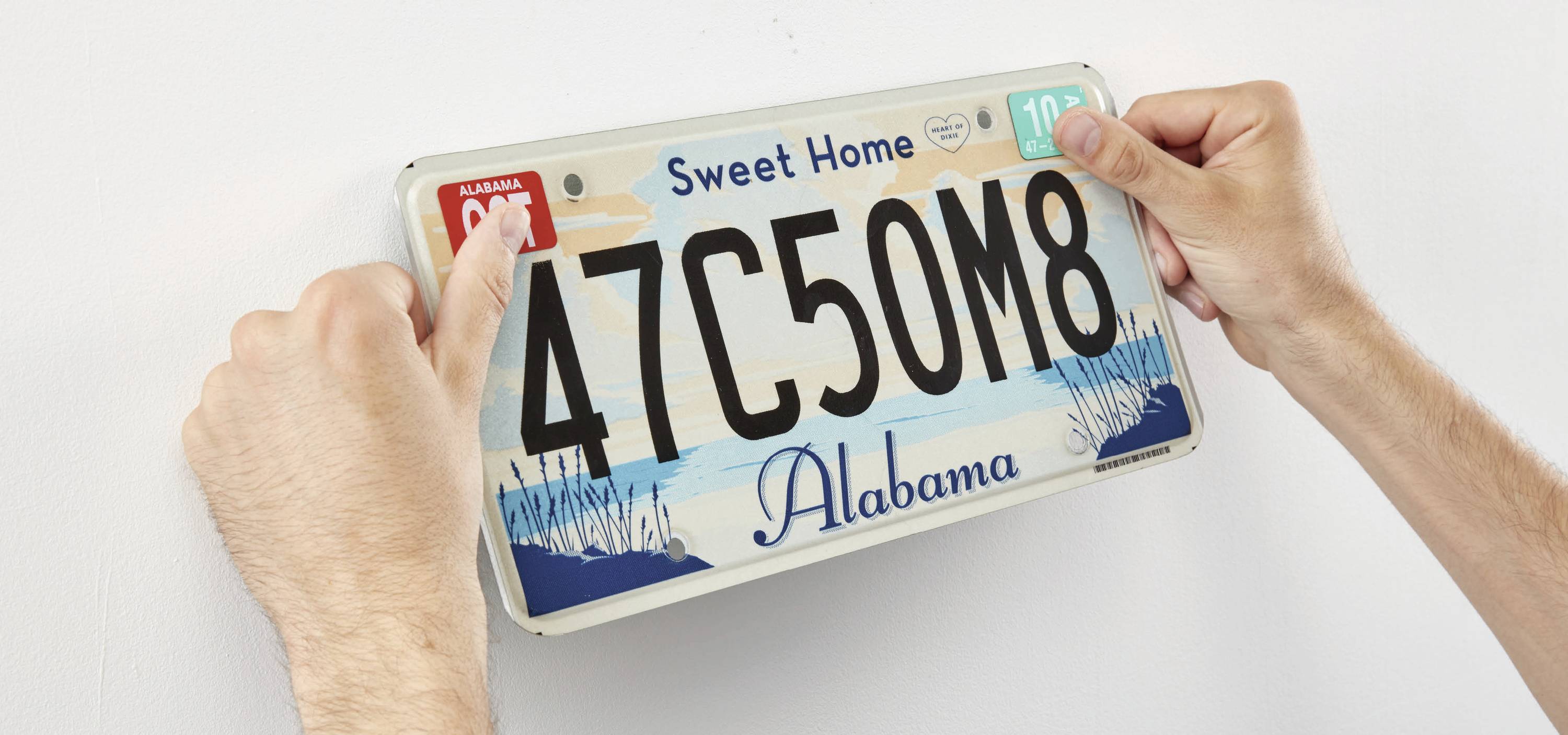 Mensch montiert ein Nummernschild mit der Aufschrift 'Sweet Home Alabama' an eine Wand.