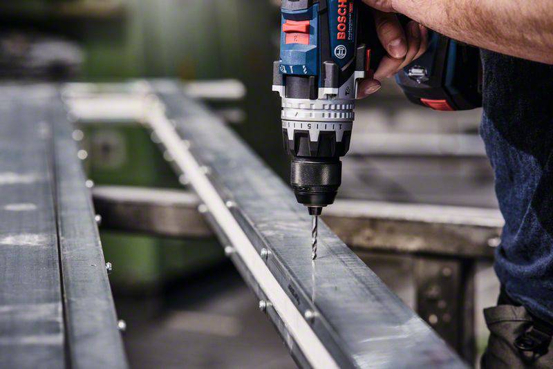 Eine Person verwendet eine elektrische Bohrmaschine, um ein Metallstück zu bohren. Der Fokus liegt auf der Bohrmaschine und dem Metall.