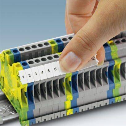 Ein Finger befestigt eine nummerierte Abdeckung auf einer grauen elektrischen Klemmenleiste, die auf einer Metallschiene montiert ist.