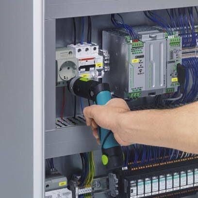 Eine Person befestigt mit einem Akkuschrauber Kabel an einer Schaltanlage. Erkennbar sind mehrere Sicherungen und elektrische Komponenten.