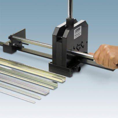Eine Hand bedient eine Metallhandhebelschere zum Schneiden von Metallstäben. Auf dem Tisch liegen verschiedene Metallstangen.