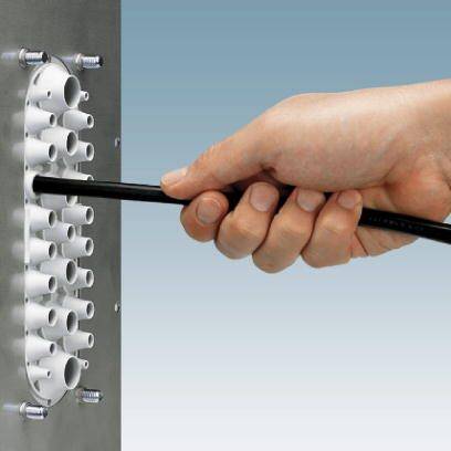 Eine Hand hält ein Kabel, das durch eine Kabeldurchführung in einer Metallplatte gesteckt wird. Die Durchführung hat mehrere Öffnungen.