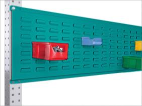 Bildausschnitt eines grünen Lochblechs mit bunten, angebrachten Aufbewahrungsboxen in Rot, Blau und Grün an einer Metallhalterung.