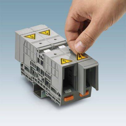 Eine Hand montiert eine graue elektrische Klemme auf einer Schiene. Gelbe Warnsymbole mit Blitz sind darauf zu sehen.