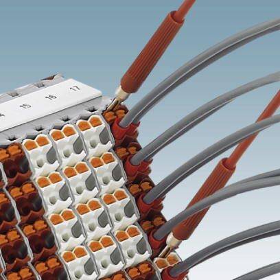 Auf einer elektrischen Klemmenleiste sind mehrere Drähte in orange und grau angeschlossen. Die Klemmen sind in Reihen angeordnet.
