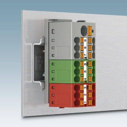 Ein elektrischer Steckverbinder mit farbcodierten Anschlüssen in Grau, Grün und Rot, montiert auf einer Metallplatte.