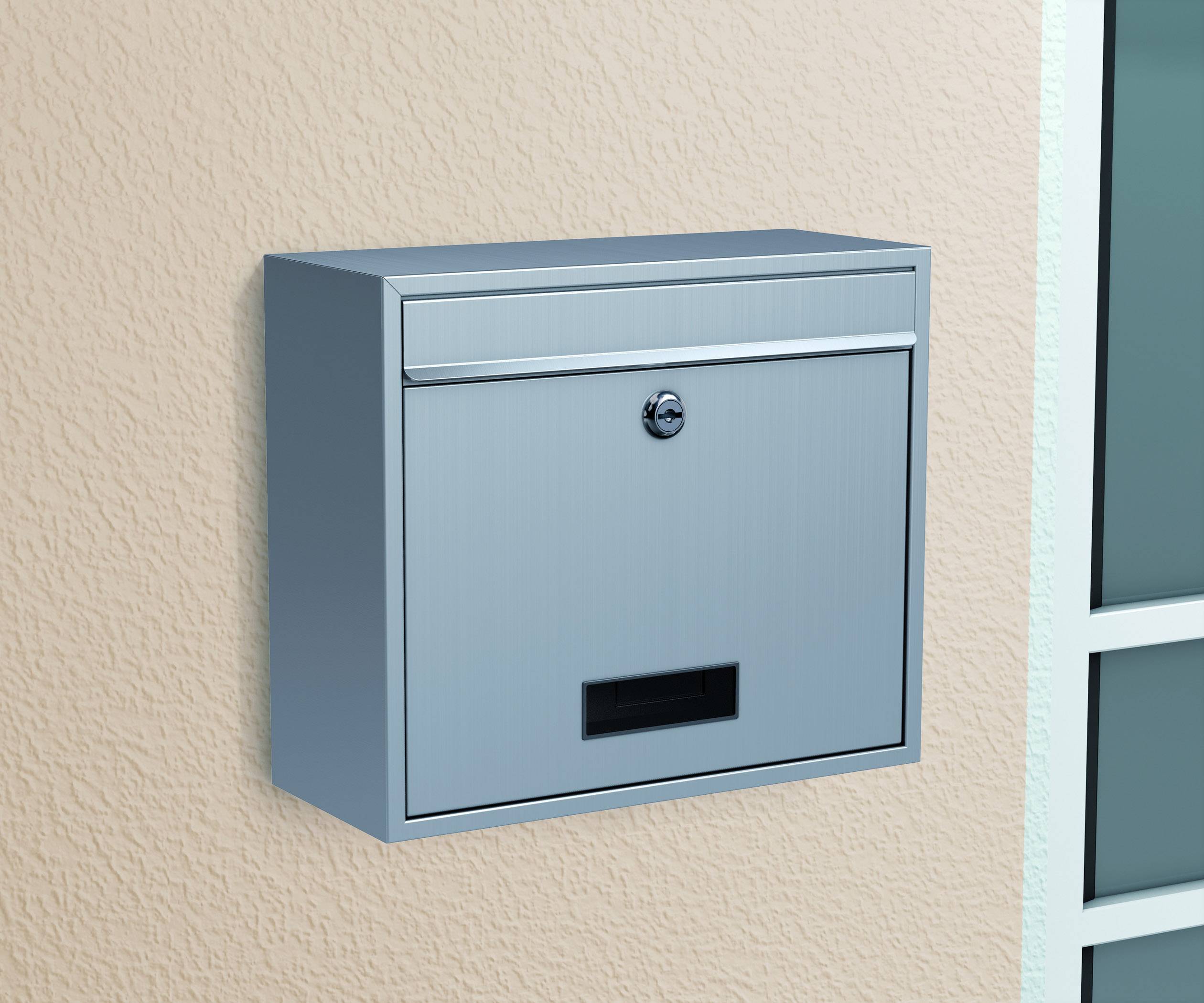 Silberner Briefkasten an einer hellen Wand montiert, mit Schloss und Namensschildhalterung.