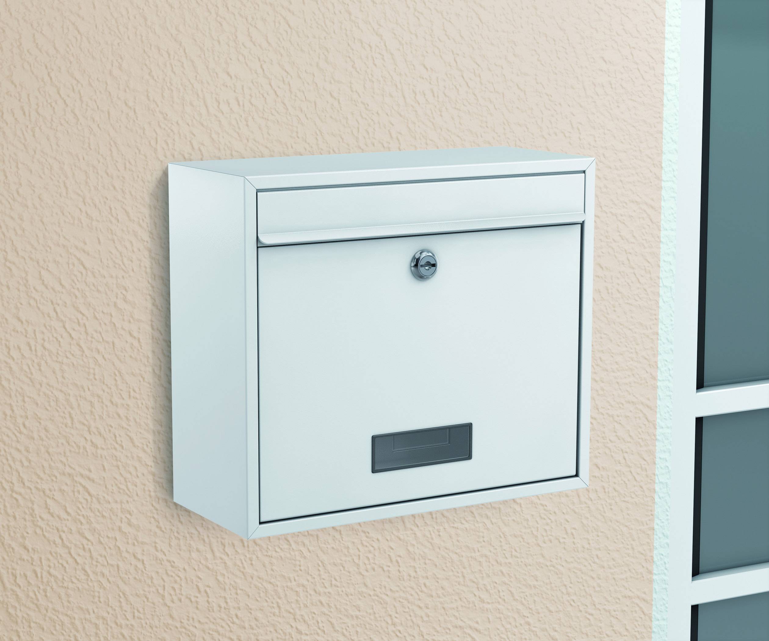 Ein weißer Briefkasten hängt an einer beigen Wand neben einem Fenster. Der Briefkasten hat einen Schlitz und ein Schloss.
