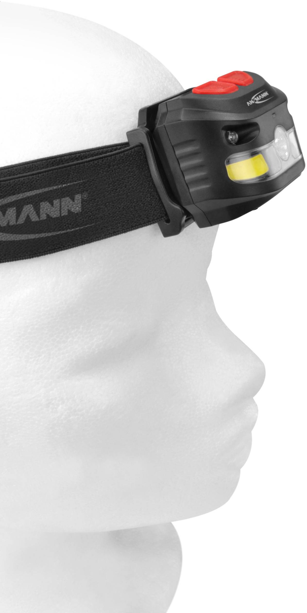 Ein Modellkopf trägt eine schwarze Stirnlampe mit einem roten Knopf, seitlicher Ansicht. Die Lampe ist auf einem schwarzen Band befestigt.