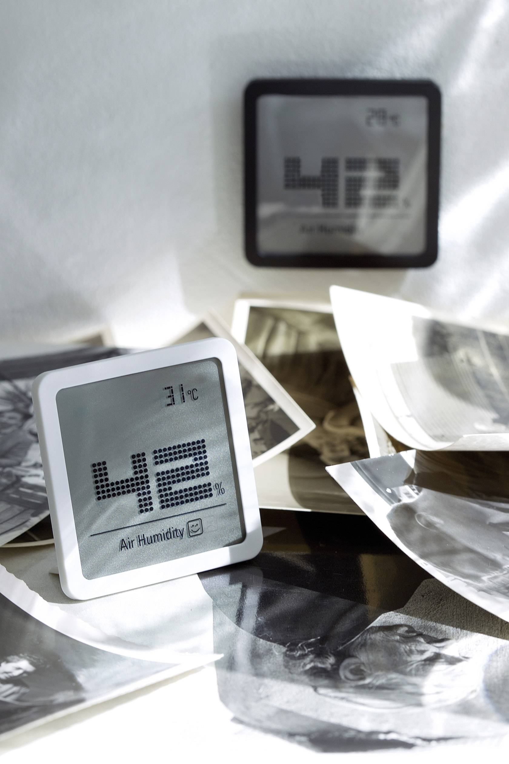 Digitales Thermo-Hygrometer zeigt 31°C und 42% Luftfeuchtigkeit an, umgeben von schwarz-weißen Fotos auf einem Tisch.