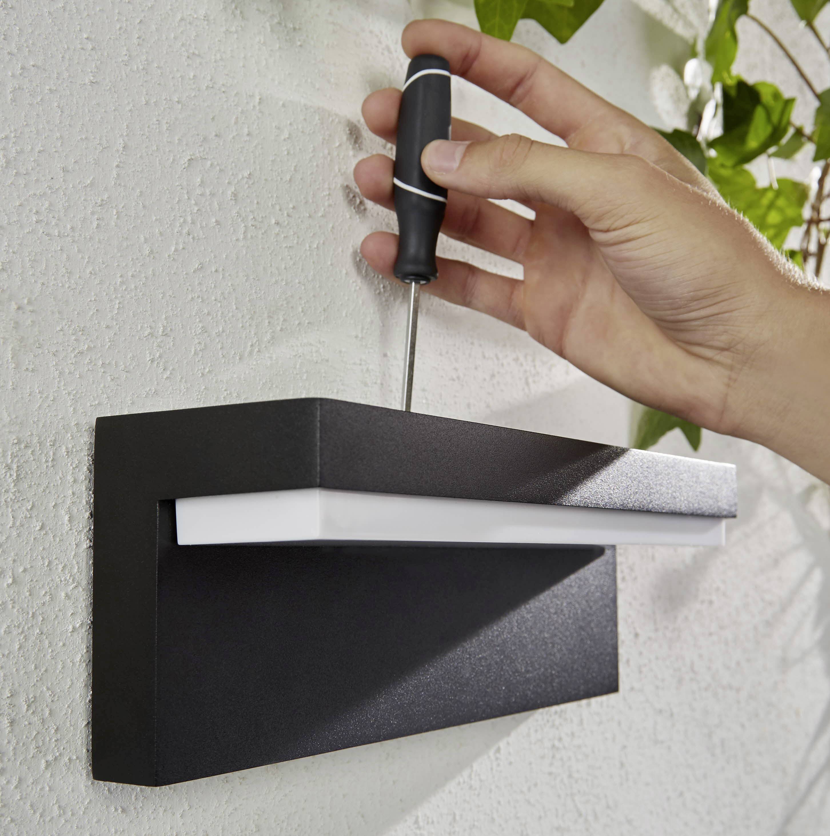 Eine Hand befestigt mit einem Schraubendreher eine schwarze Außenleuchte an einer Wand.