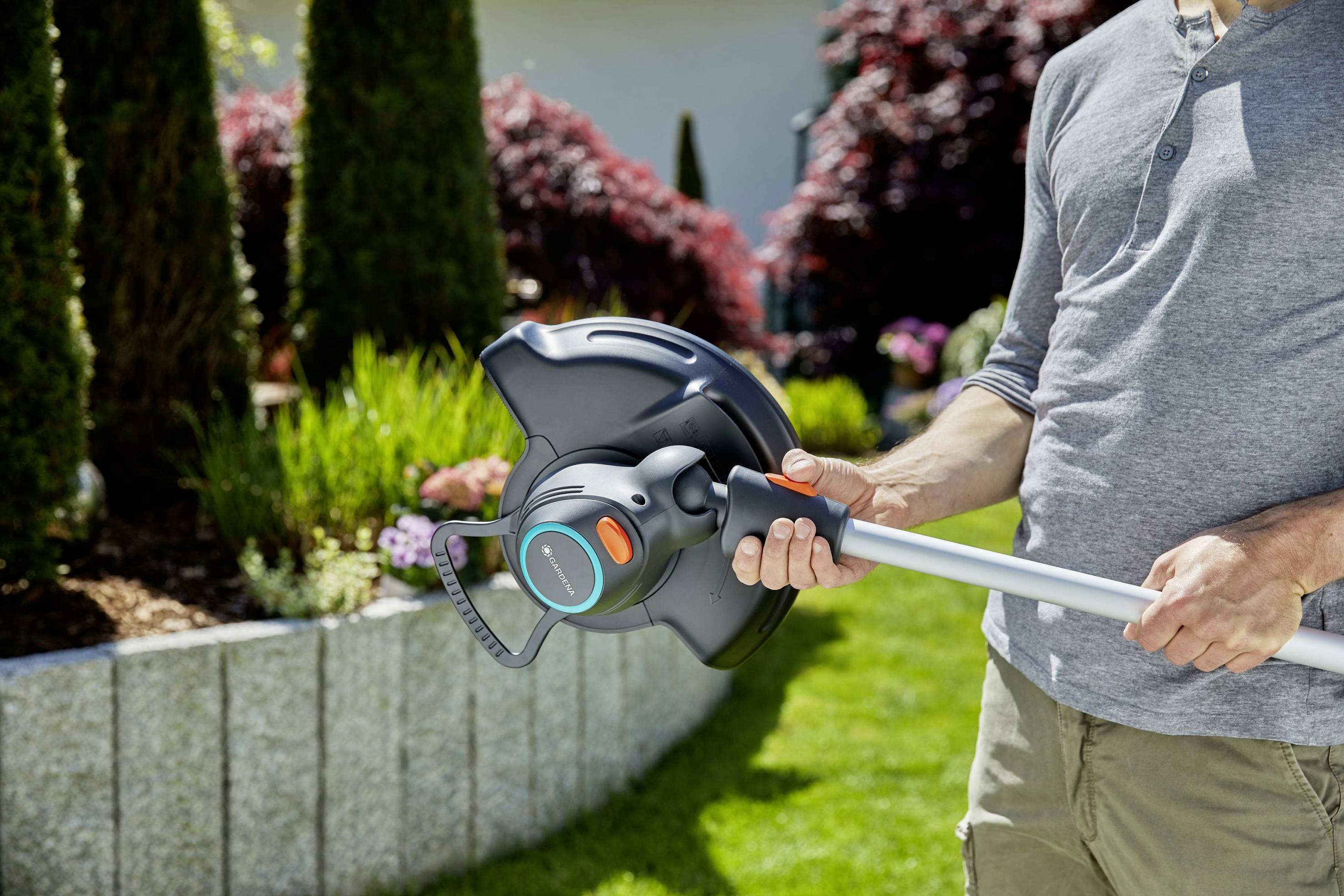 Eine Person hält einen Rasentrimmer in einem gepflegten Garten vor Blumenbeeten, bereit zum Einsatz.