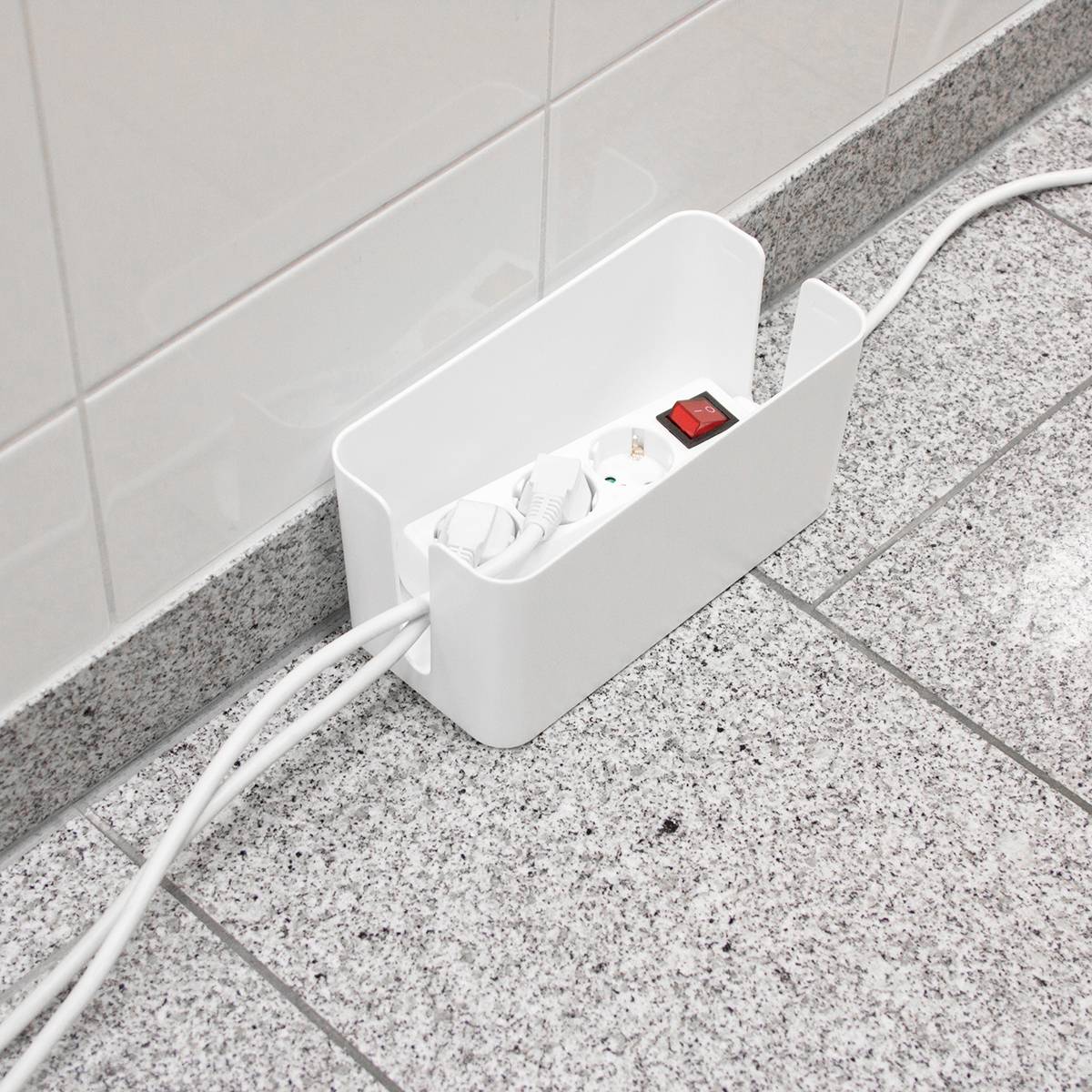 Mehrfachsteckdose in einer weißen Box auf einem gefliesten Boden. Zwei Kabel sind eingesteckt, ein roter Schalter ist sichtbar.