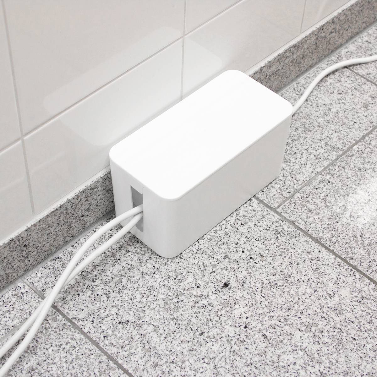 Weiße Kabelbox auf einem grauen Fliesenboden, um Ordentlichkeit zu gewährleisten. Kabel verlaufen organisiert durch die Box.