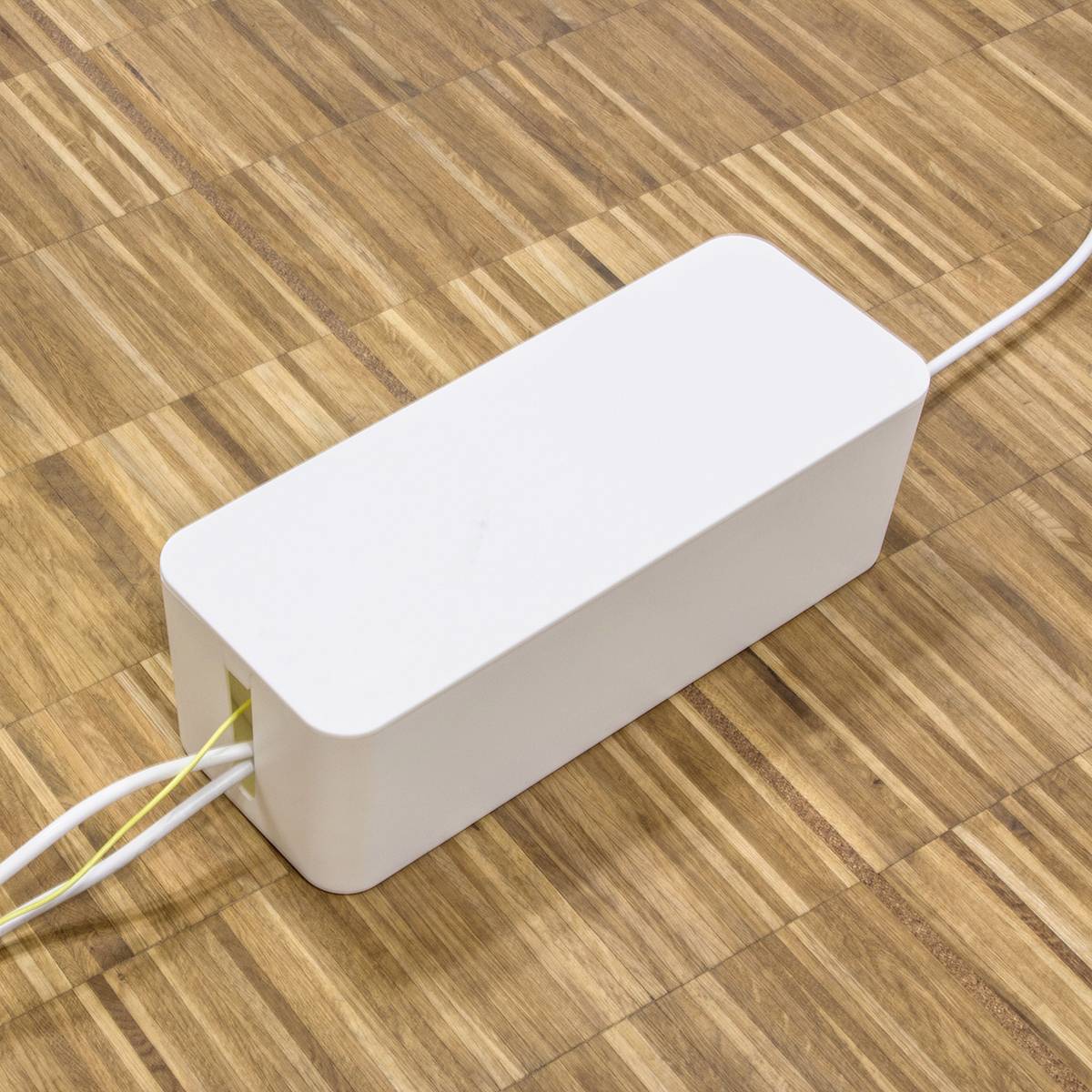 Ein weißer rechteckiger Kasten mit Kabeln liegt auf einem Holzboden. Es könnte ein elektronisches Gerät bzw. ein Adapter sein.