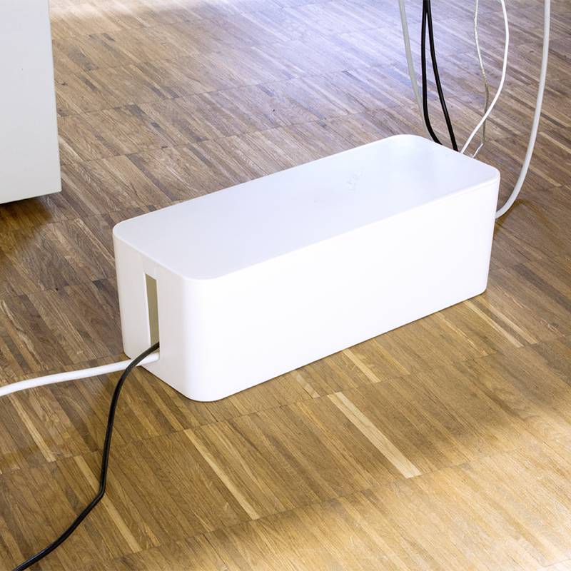 Eine weiße Kabelbox auf einem Holzboden organisiert mehrere Kabel, um Unordnung zu reduzieren und für Sicherheit zu sorgen.