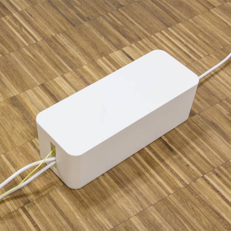 Ein rechteckiger weißer Kabelkanal auf einem Holzboden. Kabel gehen in den Kanal.