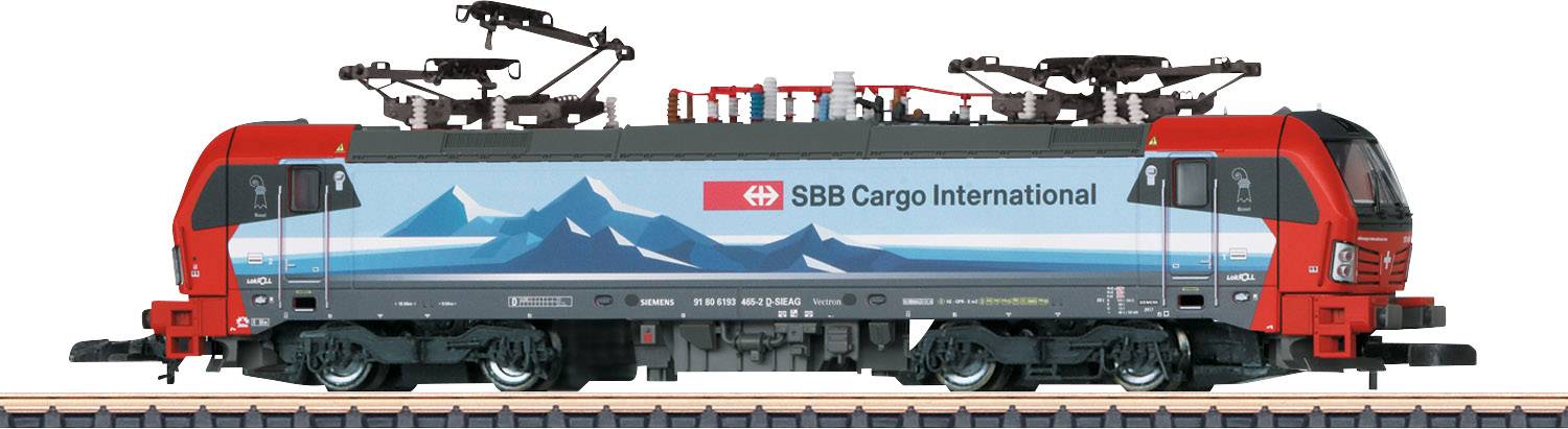 Eine rote und blaue Güterlokomotive mit der Aufschrift 'SBB Cargo International', erfolgt auf einem Gleis, dekoriert mit Bergmotiven.