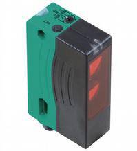 Ein rechteckiger, schwarz-grüner Sensor mit rotem Licht, wahrscheinlich ein optoelektronischer Sensor zur Objekterkennung.