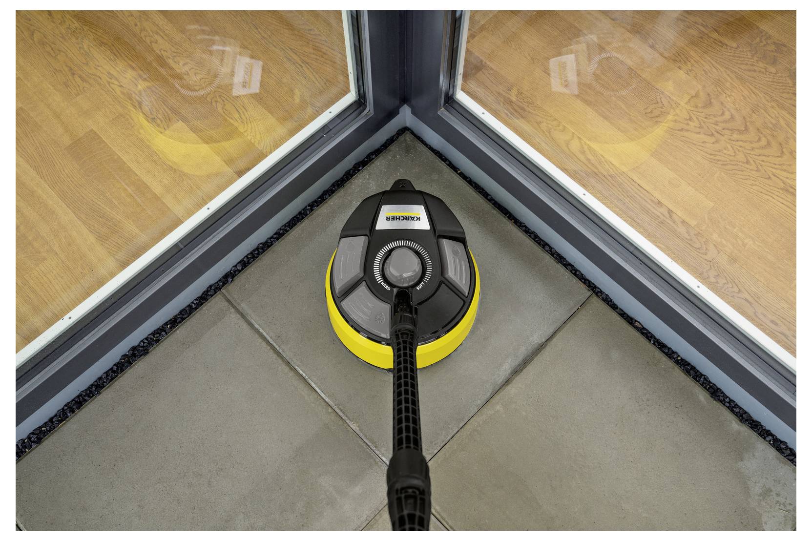 Ein Bodenreinigungsgerät wird gezeigt, wie es einen Fliesenboden in der Nähe der Ecke einer Glastür reinigt und dabei seine Fähigkeit demonstriert, Kanten effektiv zu säubern.