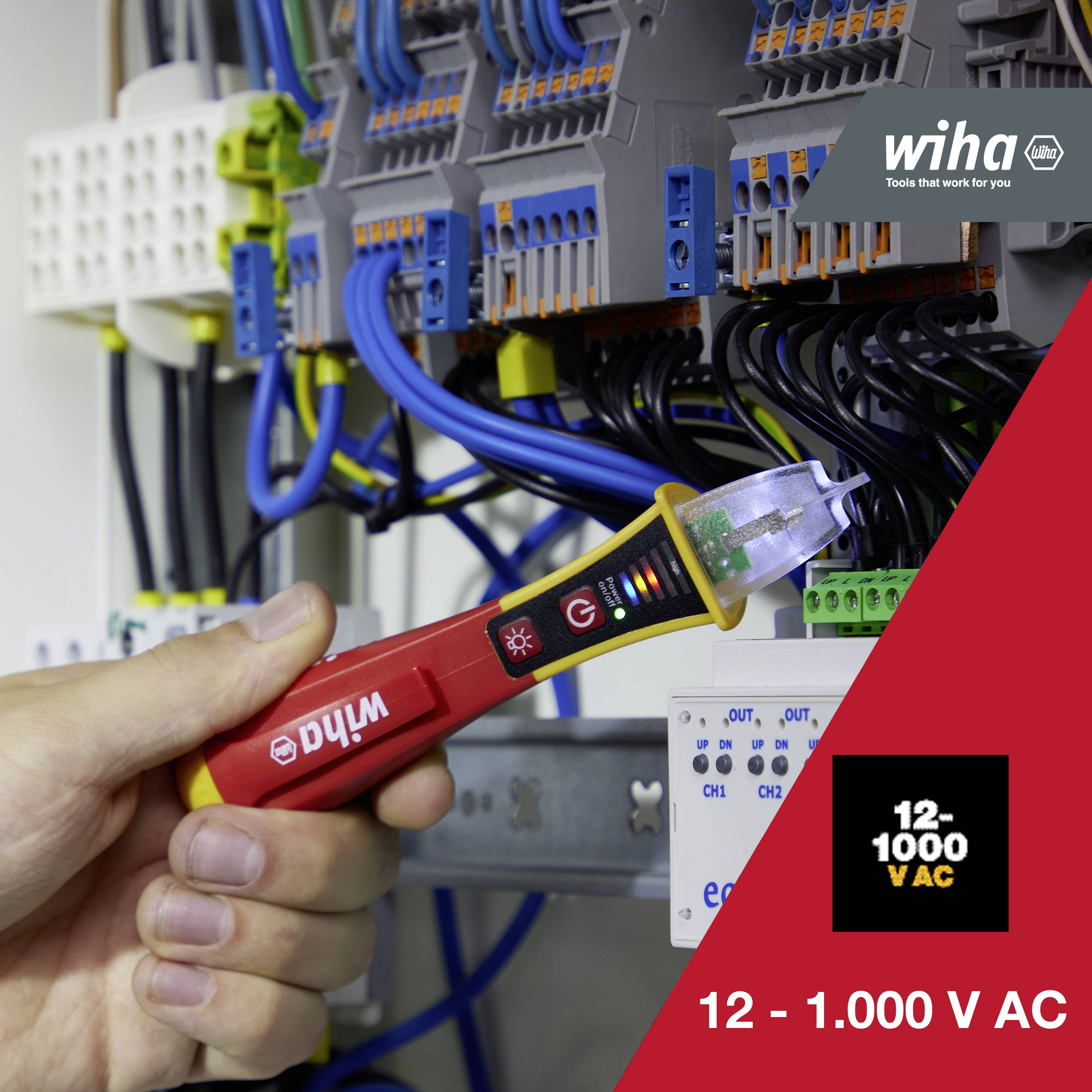 Eine Hand hält einen Spannungsprüfer vor einer elektrischen Schalttafel mit zahlreichen Kabeln, der Prüfer zeigt eine Spannung von 12 - 1.000 V AC.