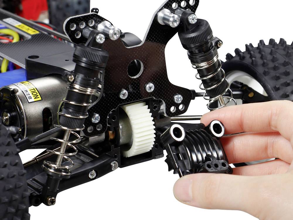 Nahaufnahme eines ferngesteuerten Buggys. Eine Hand hält Teile der Federung. Sichtbare Motor- und Getriebekomponenten.