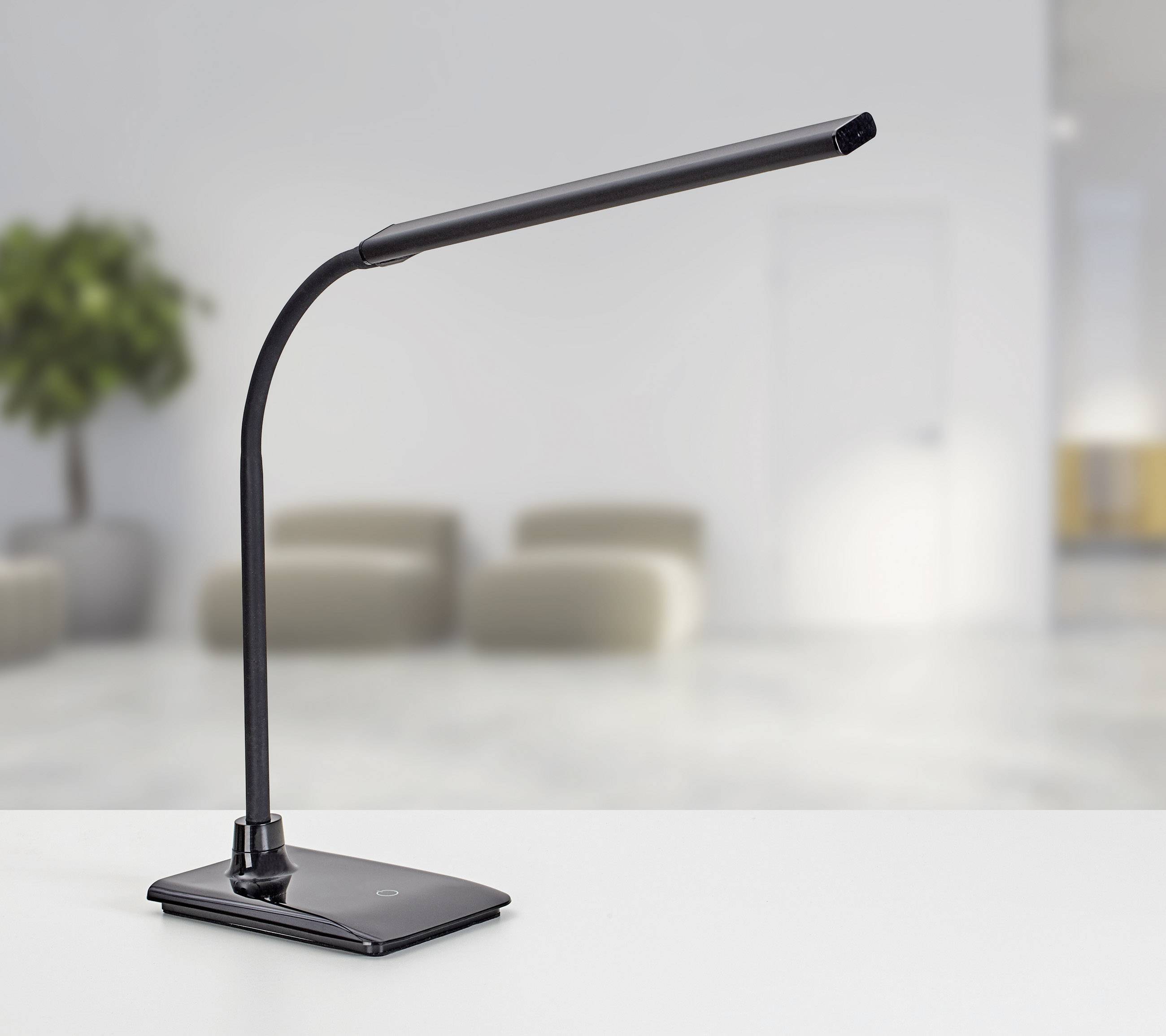 Schwarze LED-Schreibtischlampe mit flexiblem Arm steht auf einem weißen Schreibtisch in einem modernen, minimalistisch eingerichteten Raum.