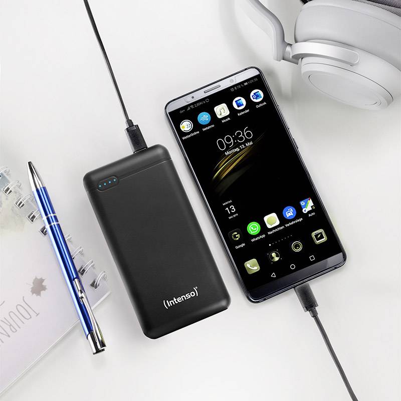 Smartphone und Powerbank laden nebeneinander. Ein Notizbuch und ein Kugelschreiber liegen daneben. Kopfhörer in der Ecke sichtbar.