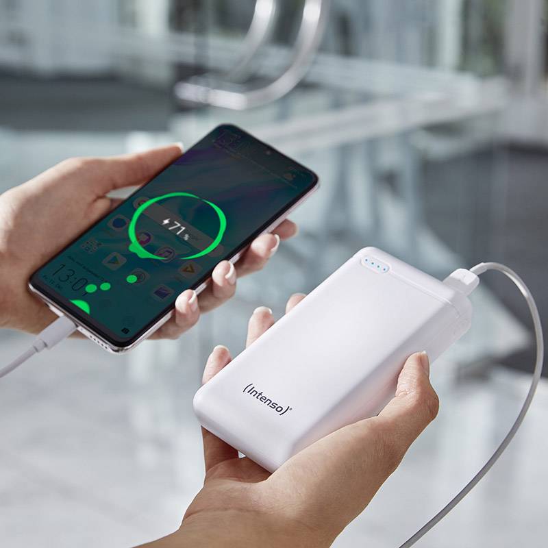Eine Hand hält ein Smartphone, das mit einer Powerbank verbunden ist, das Smartphone wird aufgeladen. Hintergrund unscharf.