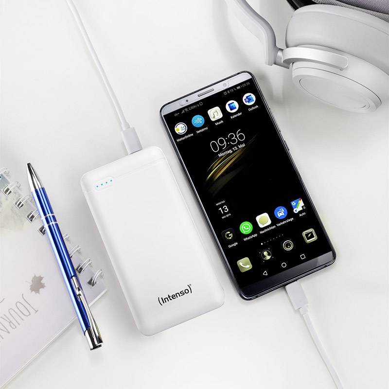 Powerbank und Smartphone mit Ladeanzeige, verbunden per Kabel auf einem Schreibtisch mit Notizbuch, Stift und Kopfhörern.