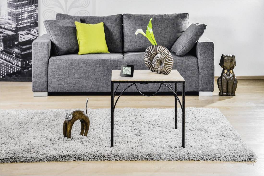Graues Sofa mit gelbem Kissen vor schwarz-weißer Wand; Holztisch mit Dekoration auf grauem Teppich; moderne Wohnzimmergestaltung.