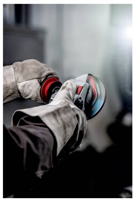 Eine Person in einer gelben Sicherheitsweste und Handschuhen benutzt einen kabellosen Bohrer an einem Metallrahmen, während Werkzeugkästen in der Nähe auf dem Boden sichtbar sind.