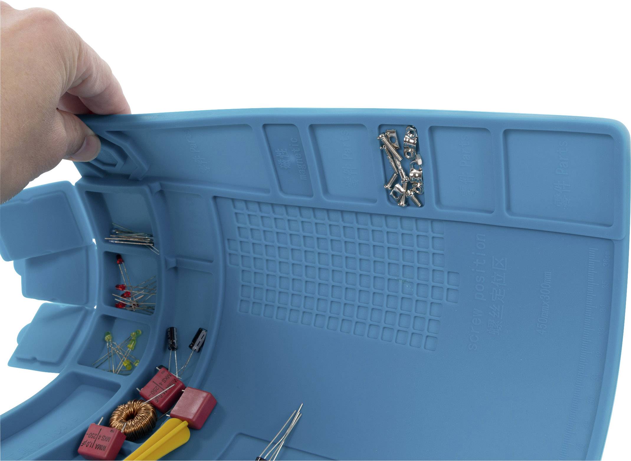 Eine Hand zeigt ein flexibles, blaues Silikon-Werkzeugtablett mit Fächern, das verschiedene kleine elektronische Bauteile enthält.