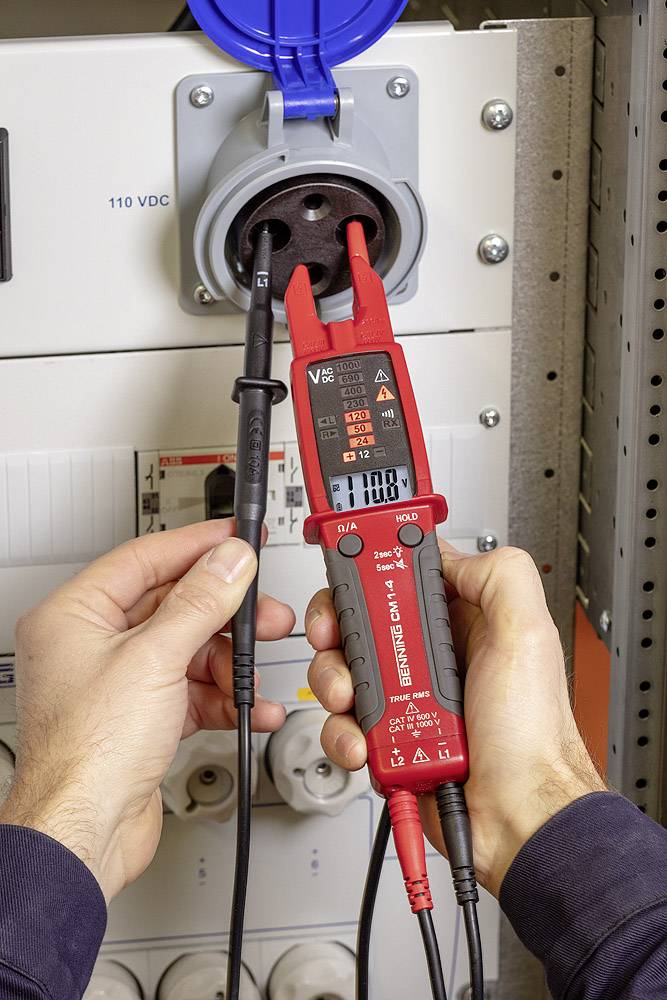 Eine Person misst die Spannung an einer Steckdose mit einem digitalen Spannungsmessgerät. Das Display zeigt 110 V DC an.