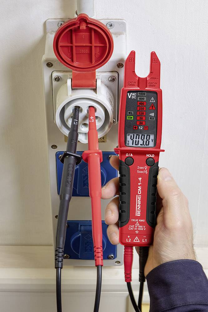 Eine Person misst mit einem Spannungsprüfer den Strom an einer Steckdose. Der Prüfgerät zeigt '230V' auf dem Display an.