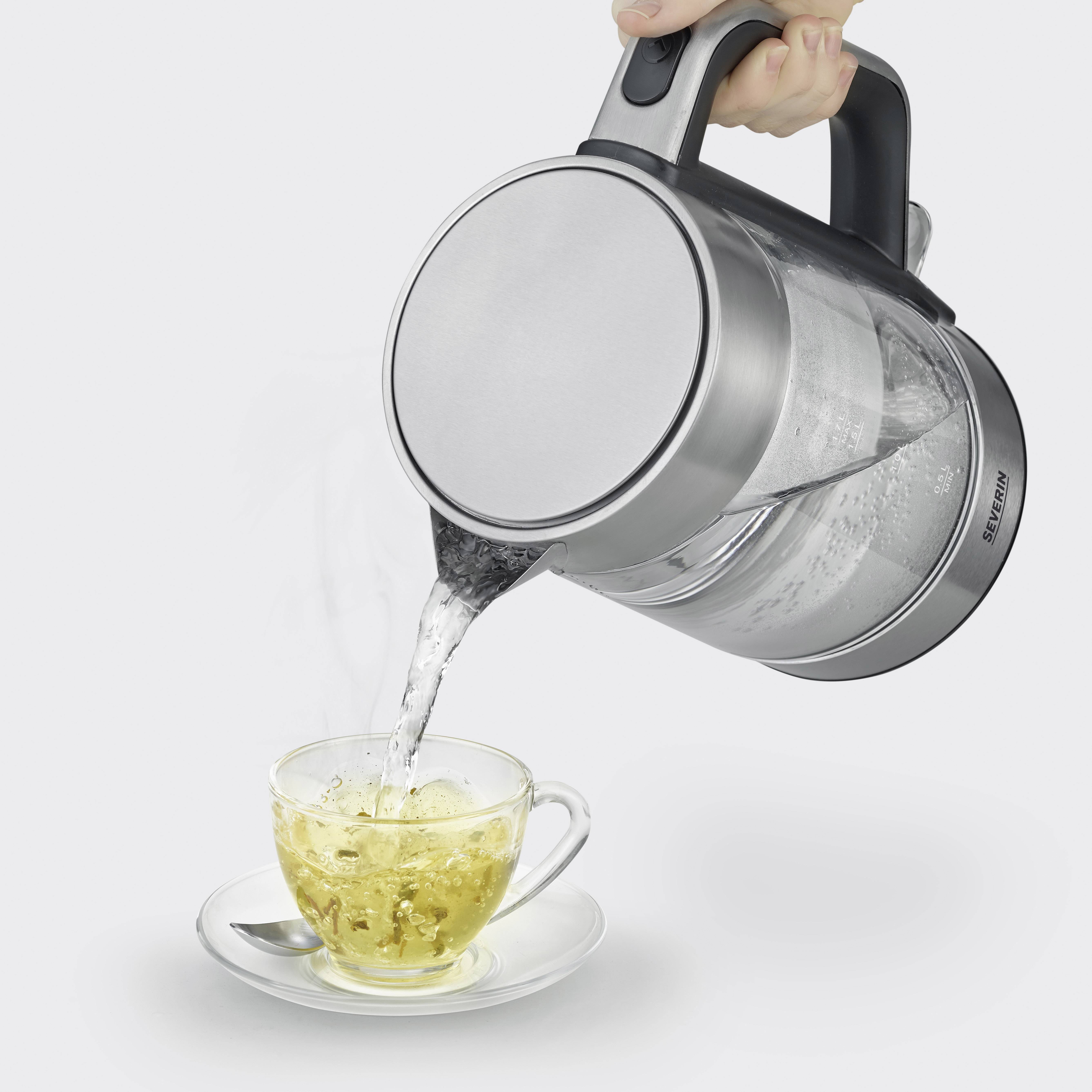 Ein Wasserkocher gießt kochendes Wasser in eine Teetasse mit Untertasse. Darin befindet sich ein Teebeutel, der Tee wird aufgebrüht.