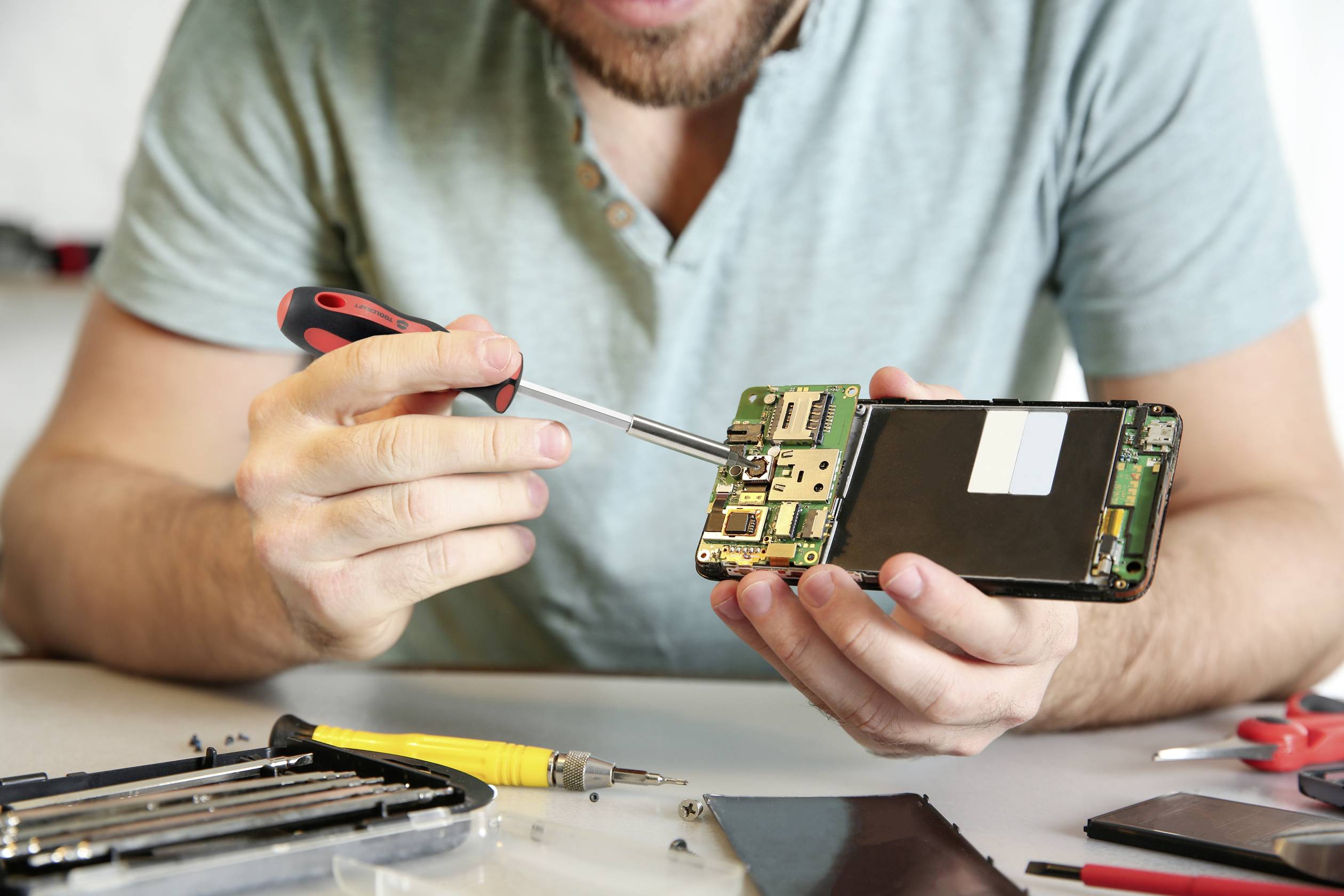 Ein Mann repariert ein Smartphone mit einem Schraubenzieher und zeigt das geöffnete Innere des Geräts.