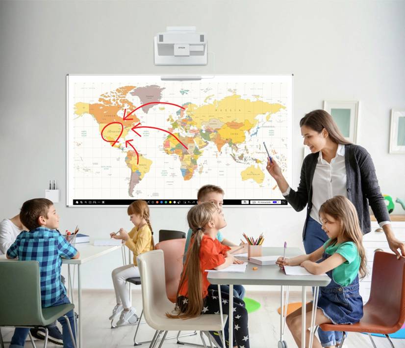 Eine Lehrerin steht vor einer Weltkarte an der Tafel und unterrichtet Kinder, die an Tischen sitzen. Arrows zeigen Richtung Nordamerika.